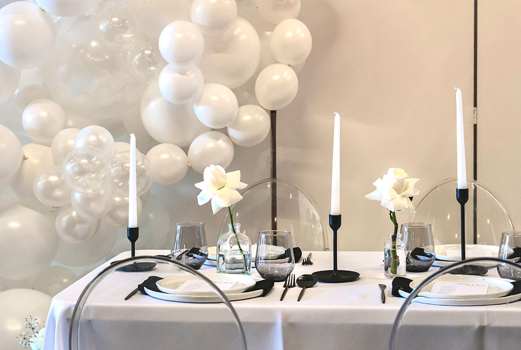 Table setting with white raised rim plates, black silverware and black taper candle holders